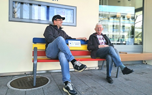 Zwei Männer lachen auf einer Bank.