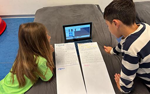 Zwei Kinder mit Papier und Laptop.