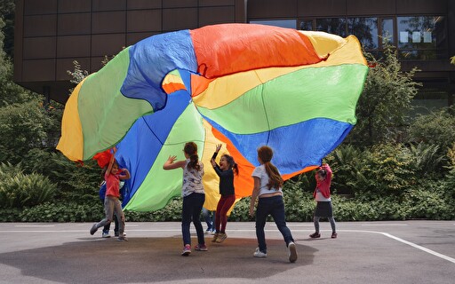 Kinder mit einem grossen, farbigen Tuch in der Luft.
