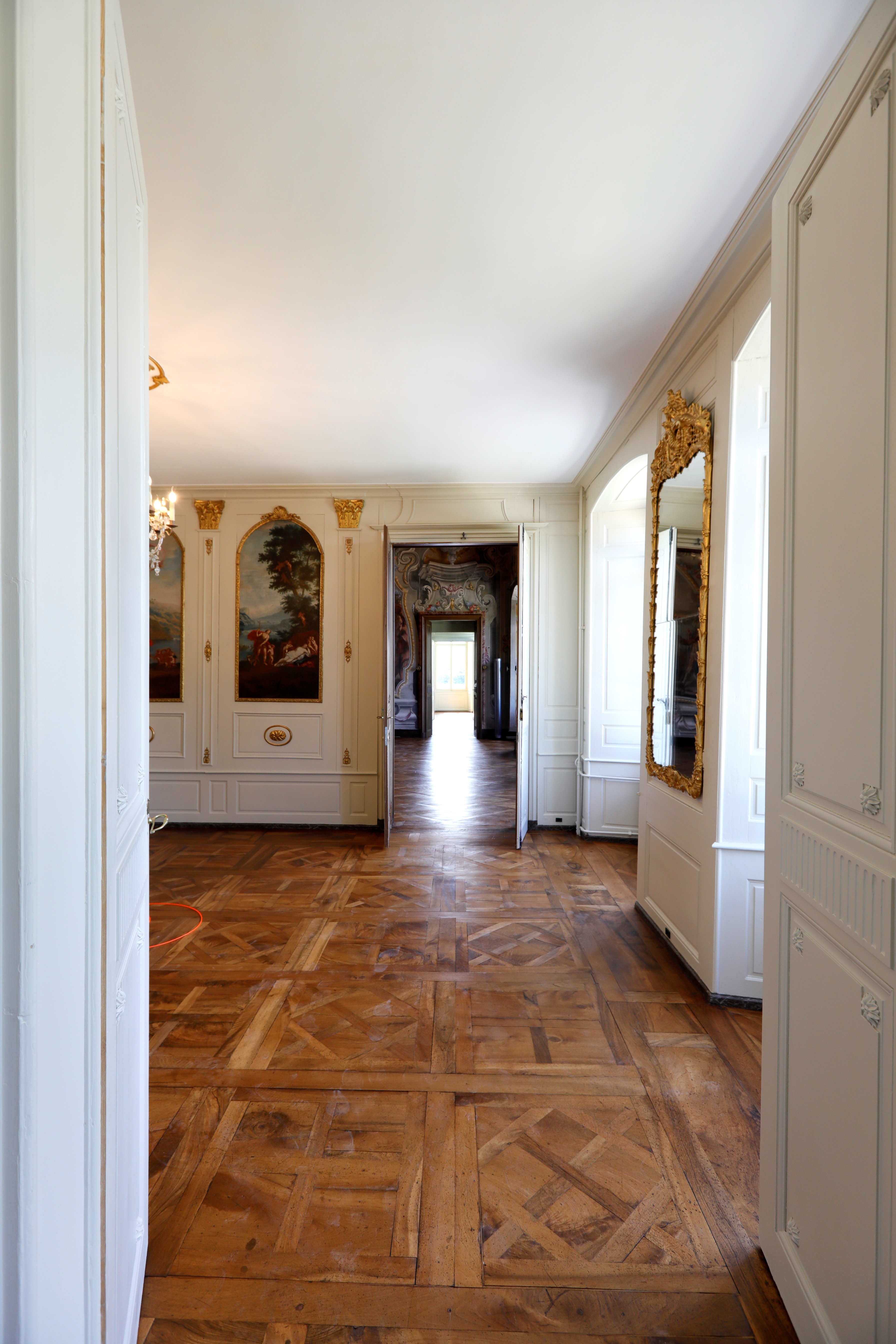 Plus l’enfilade de salons est grande, plus c’est un signe de richesse dans les châteaux du 18ème siècle. Dans le cas présent, l’enfilade se termine par un miroir qui en double la longueur.