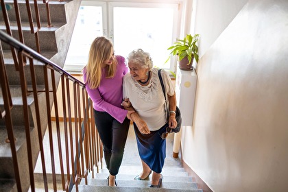 Jüngere Frau stütz ältere Dame die Treppe hoch