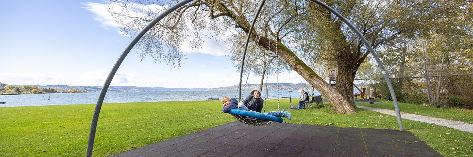 Kinder spielen auf Schaukel auf Spielplatz am See