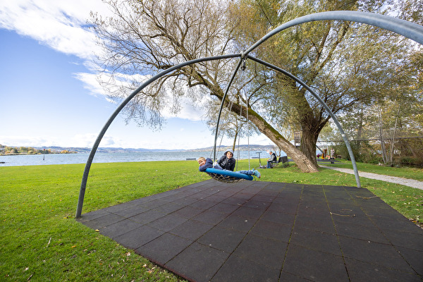 Kinder spielen auf Schaukel auf Spielplatz am See
