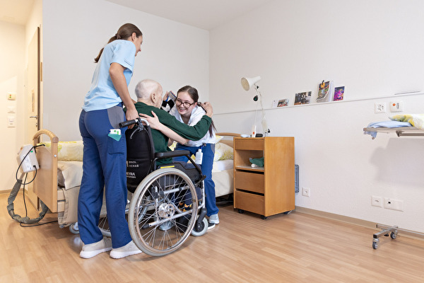 Zwei Pflegerinnen helfen Mann aus dem Rollstuhl