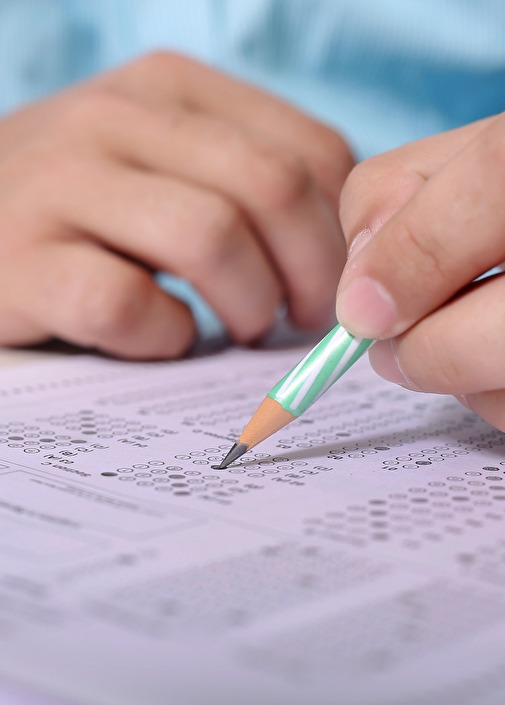 Kinderhand mit Bleistift auf Prüfungsunterlagen