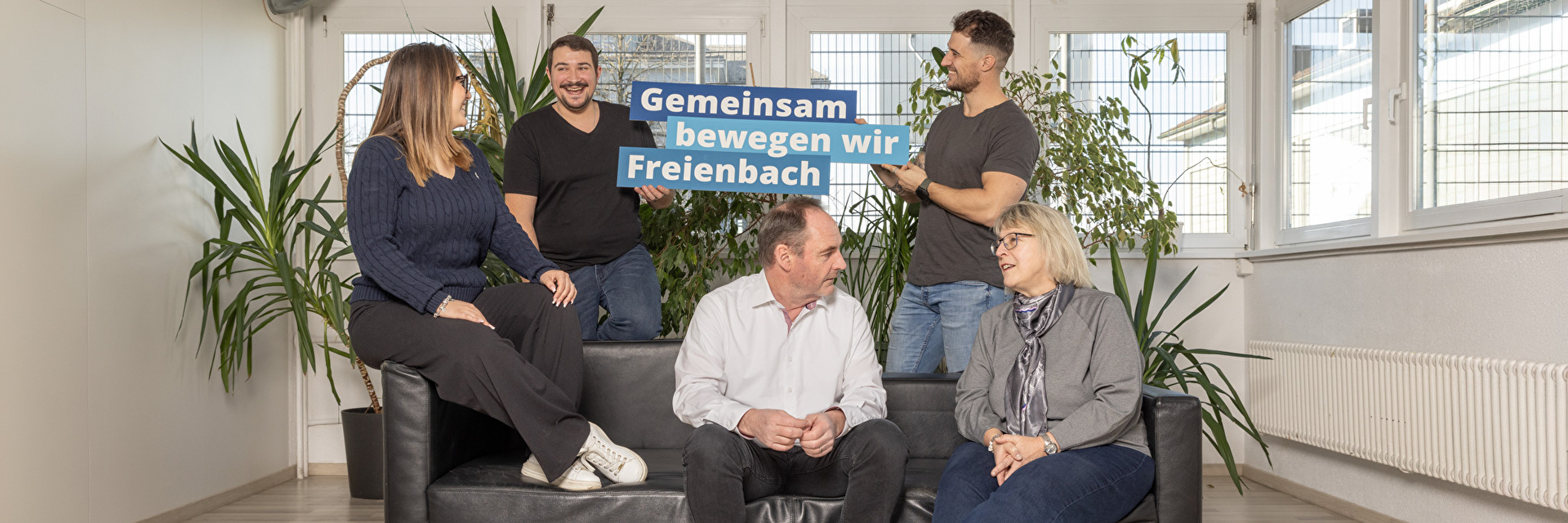 Verschiedene Mitarbeiter sitzen auf dem Sofa und Unterhalten sich in der Mitte der Claim Gemeinsam bewegen wir Freienbach