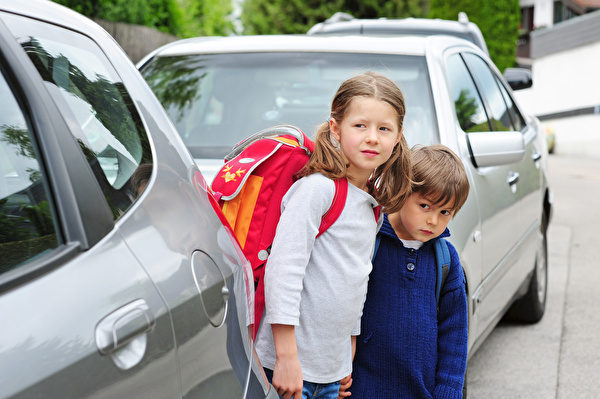 Zwei Kinder schauen zwischen Autos hervor
