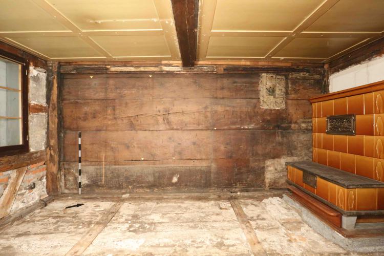Bauzeitliche Bohlenwand von 1436/37 in der Stube Kirchenstrasse 5
Auf der Wandoberfläche sind die Negative einer Sitzbank (links)
und von älteren Kachelöfen (rechts) auszumachen. In den Fugen
zwischen den Bohlen haben die Bewohner kleine Objekte
deponiert. Die Fundstellen sind mit den kleinen Dreiecken
markiert.