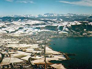 Pfeilgerade führt die Bahnlinie ins Zentrum von Zug. Im Vordergund das Quartier Riedmatt. Hinter dem Zugerberg das Panorama der Glarner Alpen.