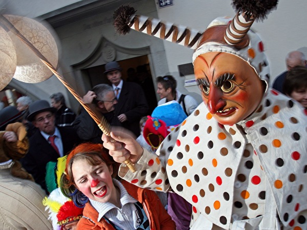 Ein Löli mit der berüchtigten Süüblatere in Aktion beim Verteilen von Würstli, Mutschli und Orangen an die Kinder, vor dem Greth-Schell-Brunnen in der Zuger Altstadt.