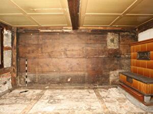 Bauzeitliche Bohlenwand von 1436/37 in der Stube Kirchenstrasse 5
Auf der Wandoberfläche sind die Negative einer Sitzbank (links)
und von älteren Kachelöfen (rechts) auszumachen. In den Fugen
zwischen den Bohlen haben die Bewohner kleine Objekte
deponiert. Die Fundstellen sind mit den kleinen Dreiecken
markiert.