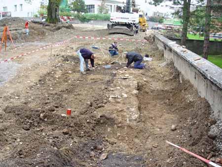 13. Oktober 2004: Das Mauerstück und zwei dunkle Erdstellen mit Skelettknochen nördlich der Mauer ziehen die Aufmerksamkeit des Archäologen-Teams auf sich.
