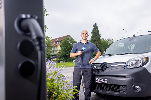 Man mit Stromkabel vor E-Ladestation