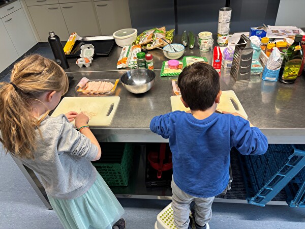 Kinder rüsten an einem Tisch fürs Mittagessen in der Betreuung.
