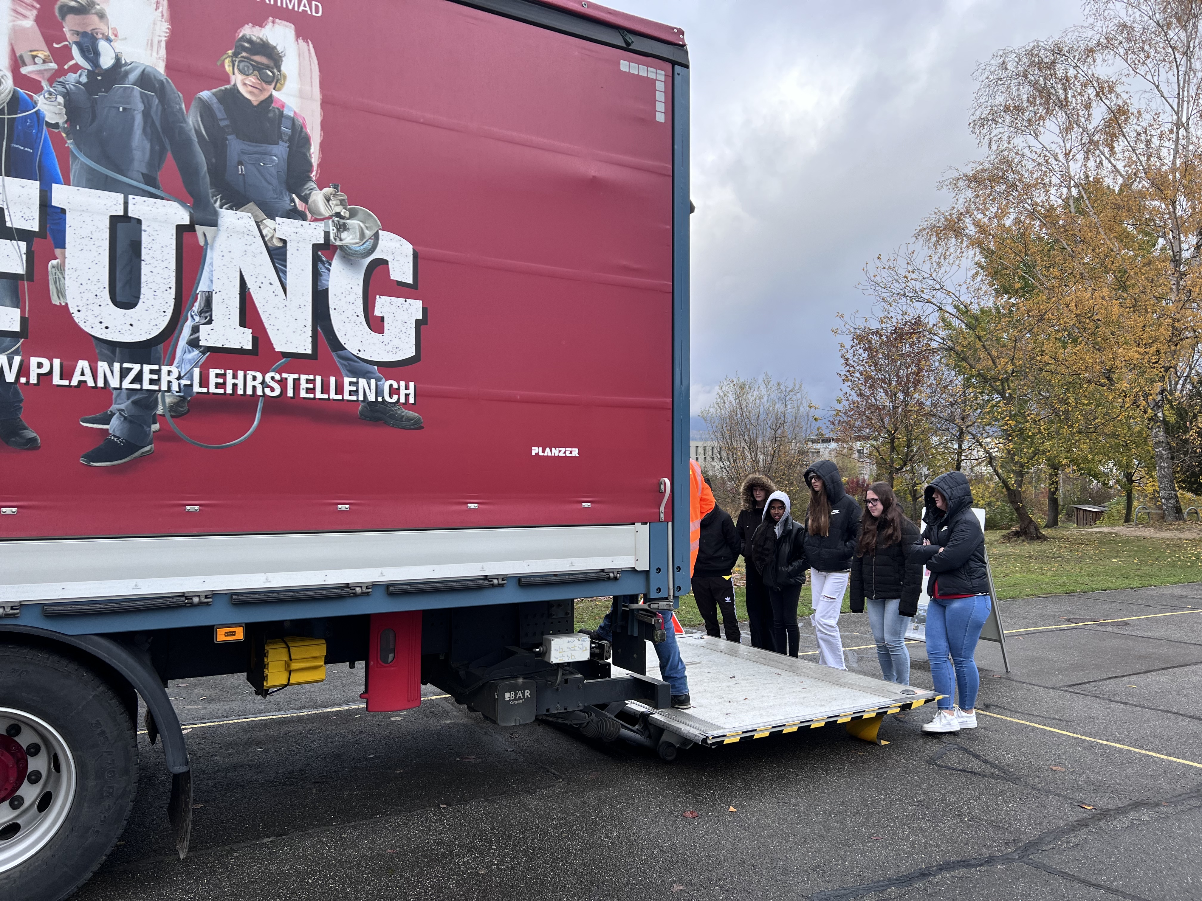 Hier gingen wir in den Lastwagen rein und schauten dort ein Video über den Totenwinkel. Die ganze Gruppe stand auf der Rampe und während dessen wurde die Rampe hochgefahren bis man problemlos auf die Laderampe standen. Drinnen haben wir auf dem Fernseher ein Video angeschaut.
