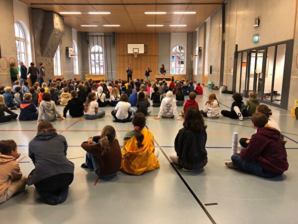 Schüler sitzen auf dem Boden in der Turnhalle