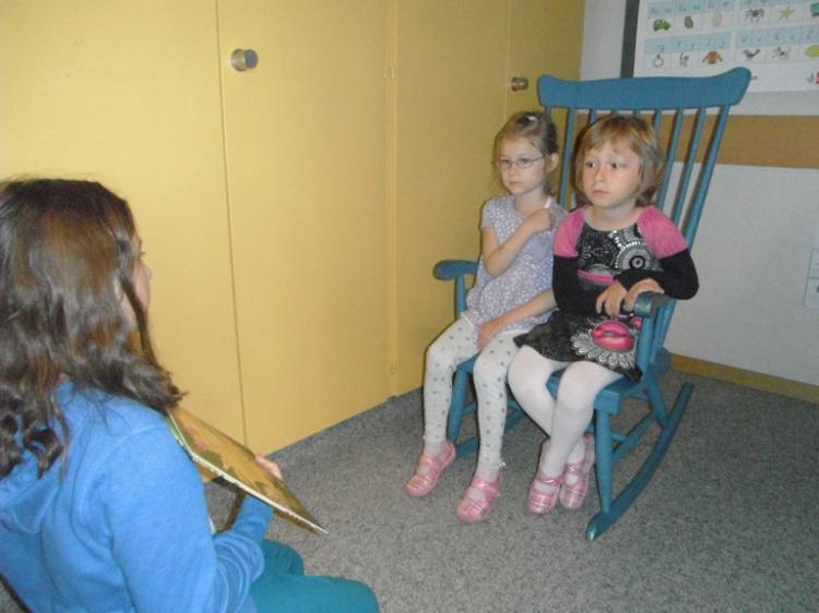 Zwei Mädchen sitzen auf einem Schaukelstuhl und hören gespannt zu.