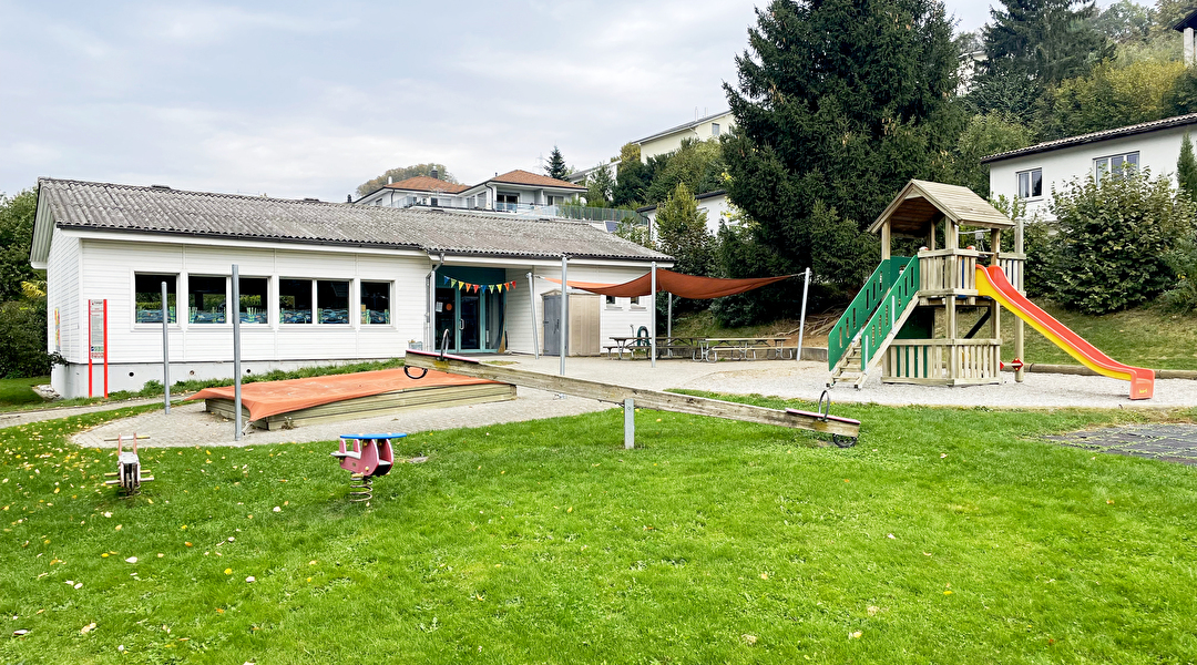 Kleiner Kindergarten mit Spielplatz davor