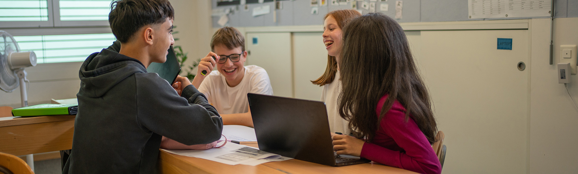 Vier Schüler diskutieren an einem Pult und zeigen sich Dinge auf dem Laptop