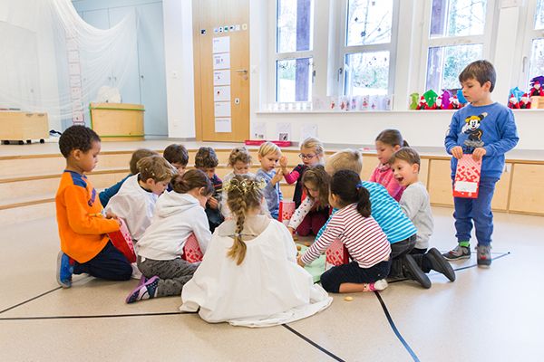 Kindergartenkinder knien am Boden im Kreis und spielen, einige Kinder sind verkleidet