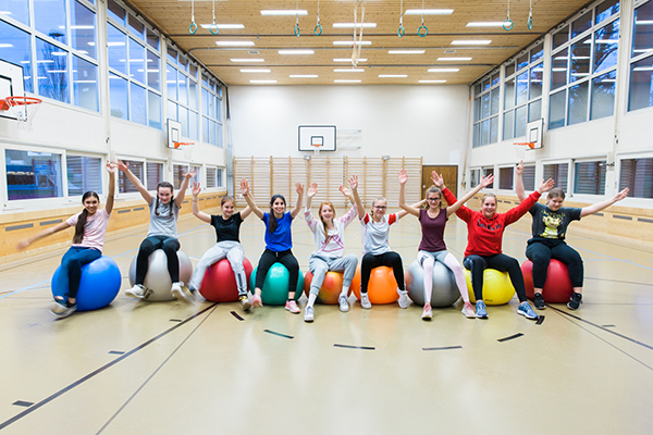 Mädchen sitzen auf Gymnastikbällen und halten die Hände in die Höhe