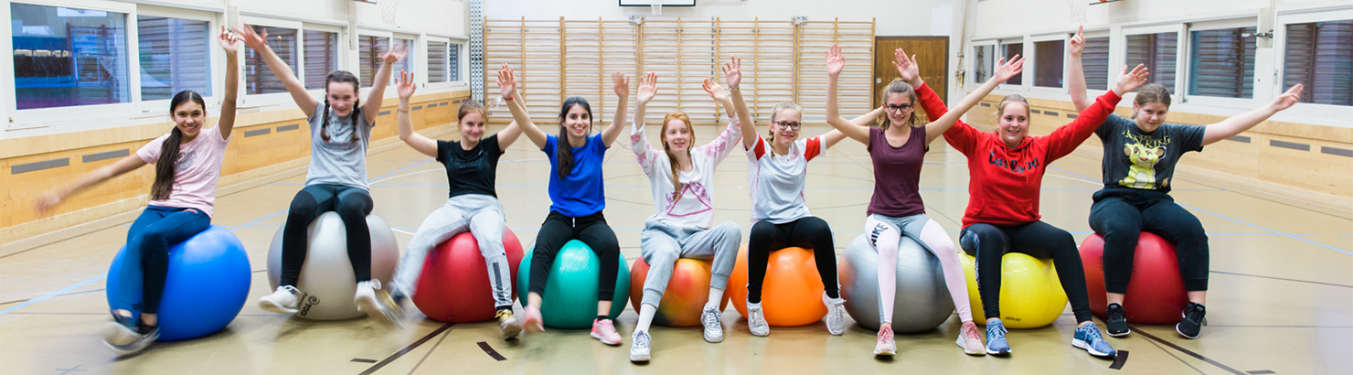 Mädchen sitzen auf Gymnastikbällen und halten die Hände in die Höhe