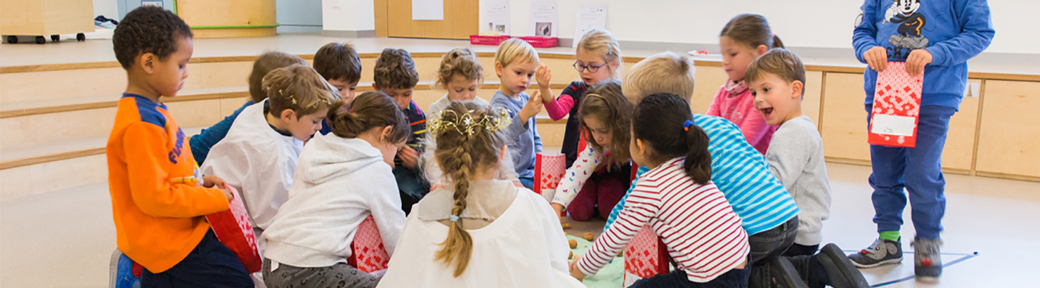 Kindergartenkinder knien am Boden im Kreis und spielen, einige Kinder sind verkleidet
