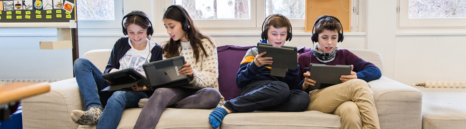 Schülerinnen und Schüler sitzend auf dem Sofa mit iPads in der Hand