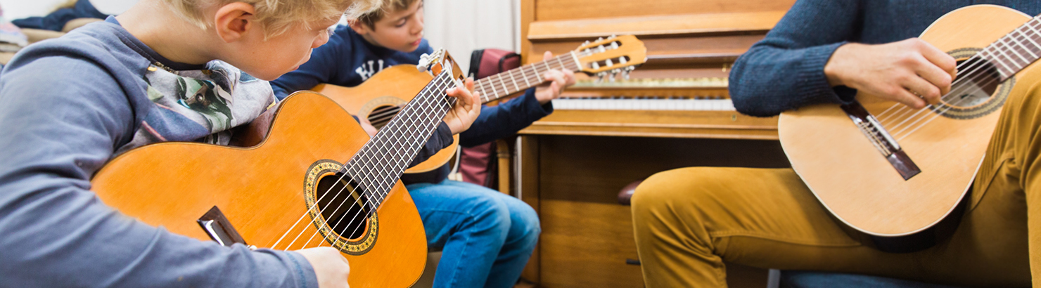 zwei Kinder am Gitarre spielen, begleitet vom Gitarren Lehrer
