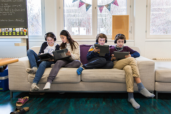 Schülerinnen und Schüler sitzend auf dem Sofa mit iPads in der Hand