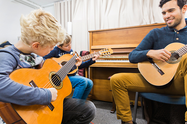 zwei Kinder am Gitarre spielen, begleitet vom Gitarren Lehrer