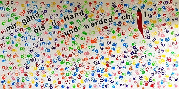 Bild von vielen farbigen Handabdrücken und dem Schriftzug mir gänd öis d'Hand und werdet chili