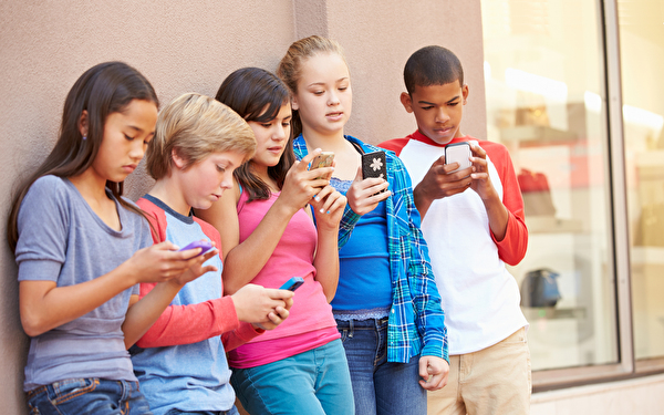 Fünf Jugendliche lehnen sich an eine Wand und schauen alle auf ihre Smartphones.