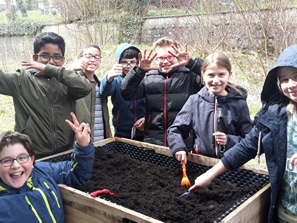 Kinder posieren hinter Hochbeet