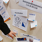 verschiedene Zettel an einem Steckboard. Finger tippt auf einen Zettel