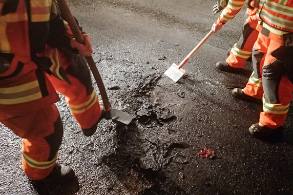 Die Feuerwehr kratzt geschmolzene Kunststoff- und Leichtmetallteile von der Fahrbahn.