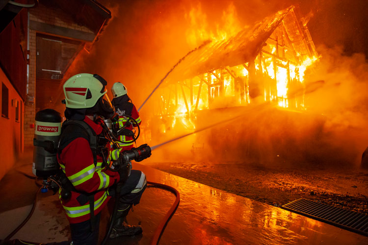 Feuerwehrleute unter Atemschutz verhindern das Übergreifen des Feuers auf Nachbargebäude.