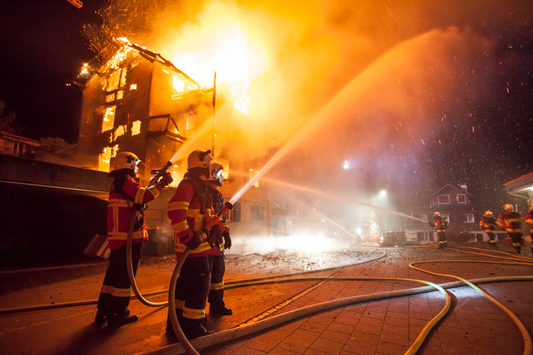 Mit Wasser kühlen Feuerehrleute die Umgebung des brennenden Wohnhauses.