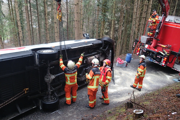 Mittels Seilzug und Kran stellt die Strassenrettungsgruppe einen Lieferwagen am Mueterschwandenberg wieder auf die Räder. Ausserdem muss die Feuerwehr ein Leck abdichten und die Strasse von ausgelaufenem Öl reinigen.