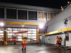 An der zum Leiterhebel umfunktionierten Leiter lassen die Feuerwehrleute eine Rettungspuppe in der Korbtrage waagrechten in die Tiefe.