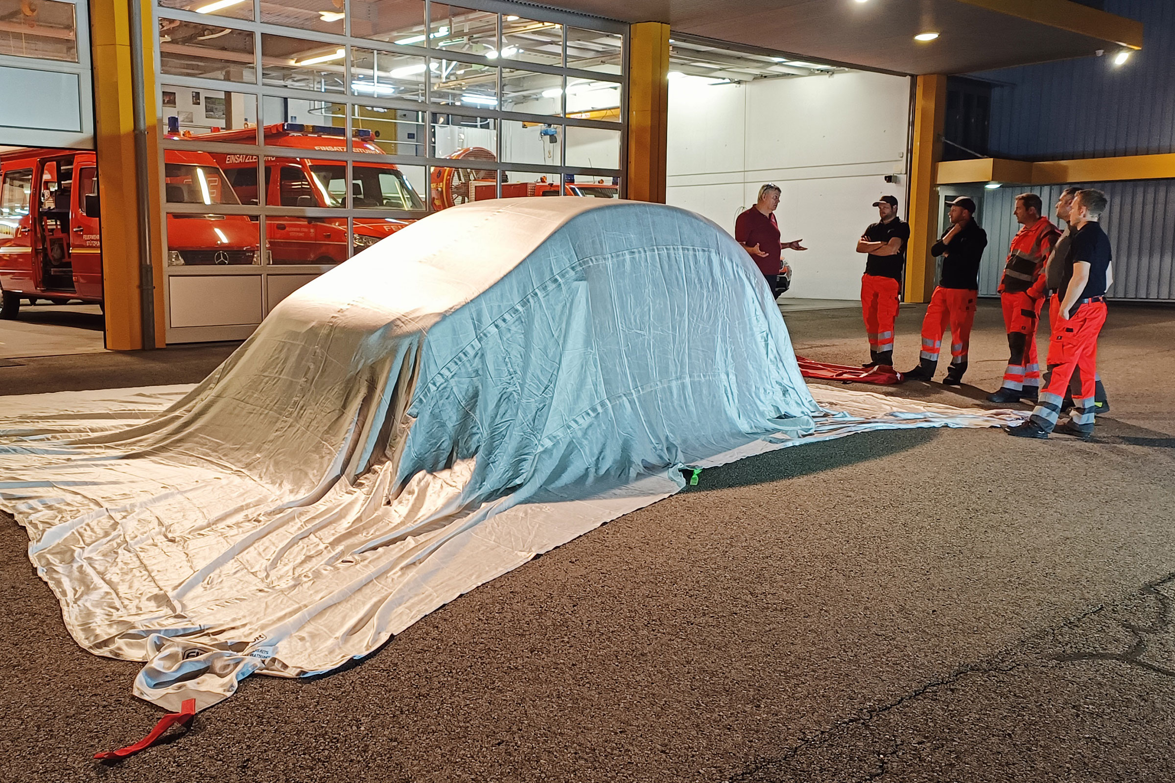 An einer Atemschutzprobe wird eine Löschdecke vorgestellt, die ein ganzes Auto abdeckt.