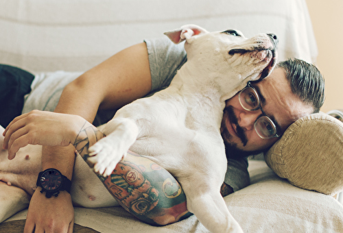 Ein tätowierter Mann liegt mit seinem Hund auf dem Sofa.