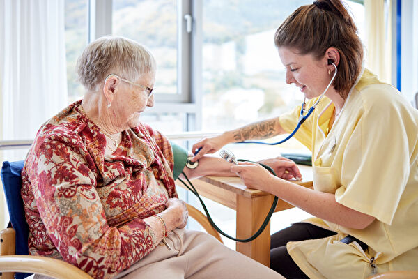 Eine ausgebildete Pflegefachfrau misst den Puls am Arm einer Bewohnerin.