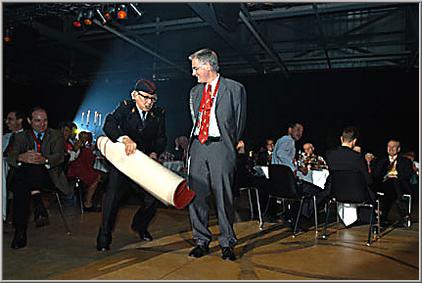 Herr Regierungsrat Hanspeter Uster wird von Archiblad Brändli auf die Bühne geführt. Der rote Teppich wird verlegt.